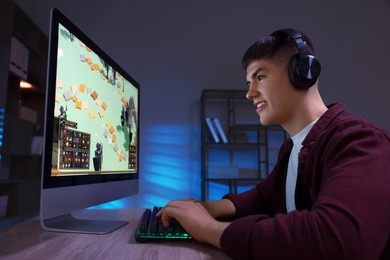 Young man playing video game with keyboard at wooden table indoors