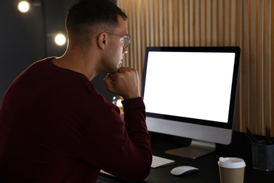 Photo of Man using computer monitor at table indoors