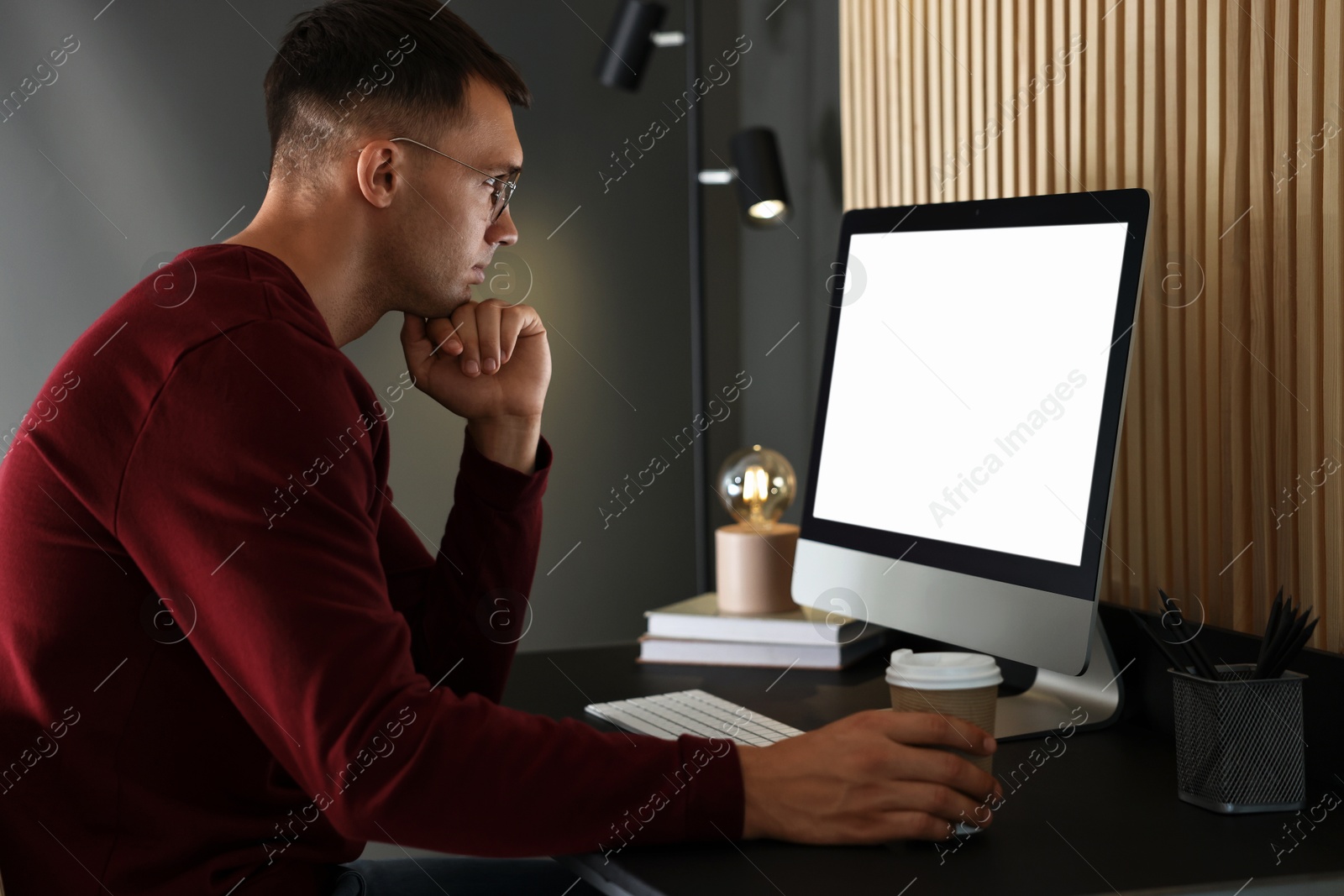 Photo of Man with drink using computer monitor at table indoors