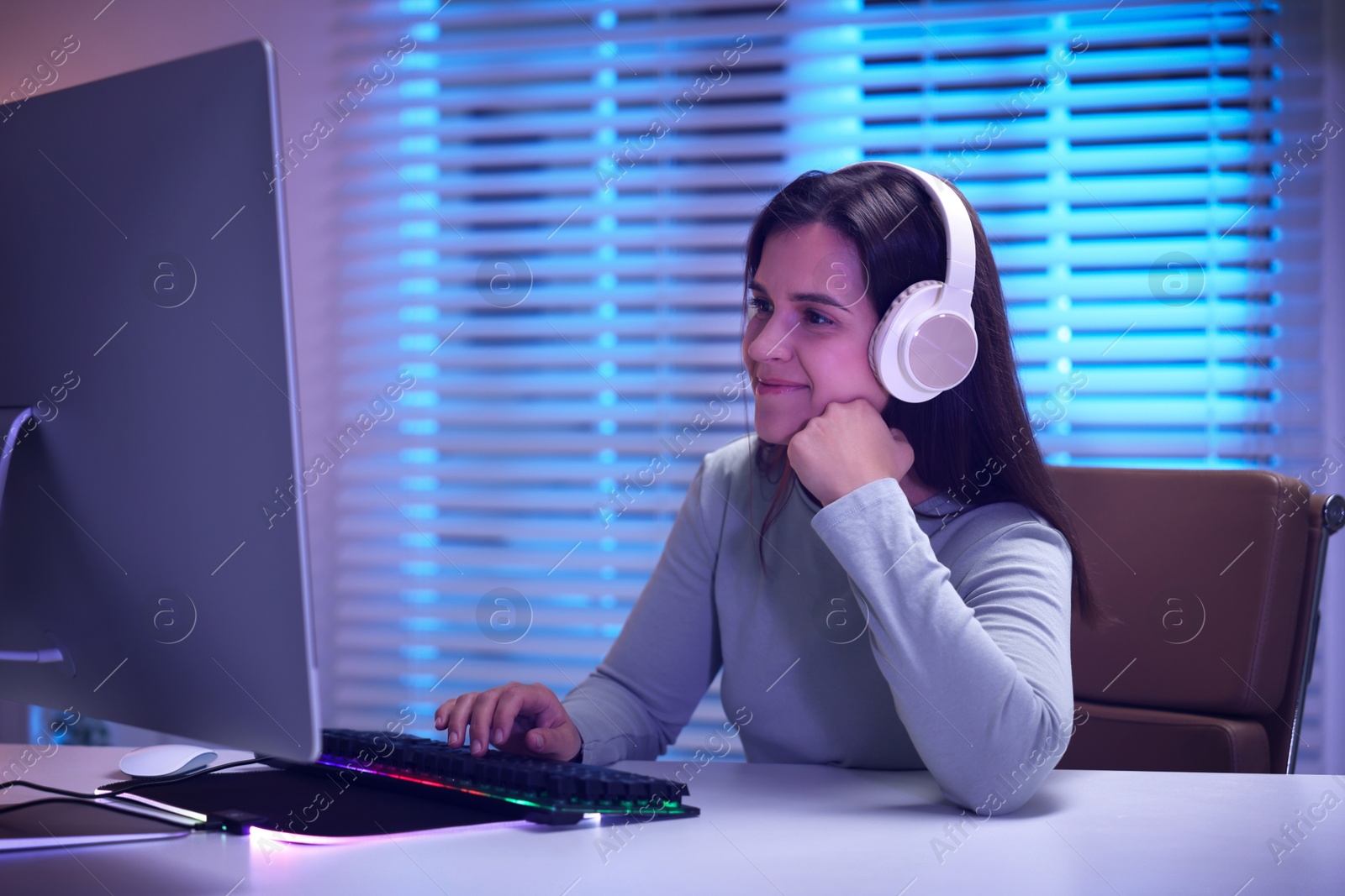 Photo of Woman in headphones playing video game with keyboard at table indoors