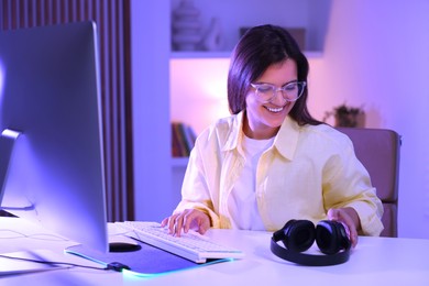 Smiling woman taking headphones from table with keyboard and monitor indoors