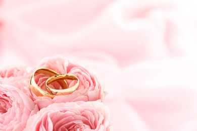 Golden wedding rings and flowers on blurred background, closeup. Space for text