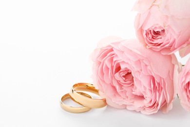 Photo of Golden wedding rings and flowers on white background, closeup. Space for text