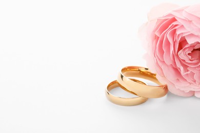 Photo of Golden wedding rings and flower on white background, closeup. Space for text