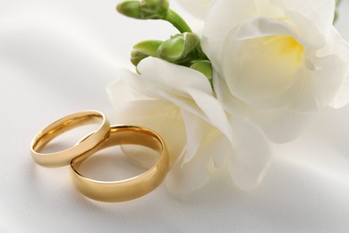 Photo of Golden wedding rings and flowers on white fabric, closeup