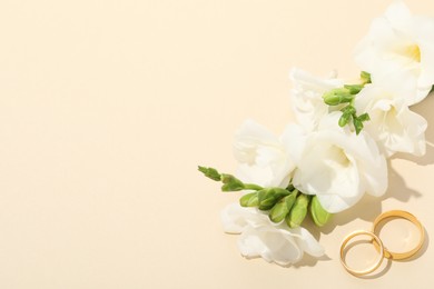 Photo of Golden wedding rings and flowers on beige background, above view. Space for text