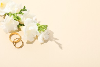 Photo of Golden wedding rings and flowers on beige background, space for text