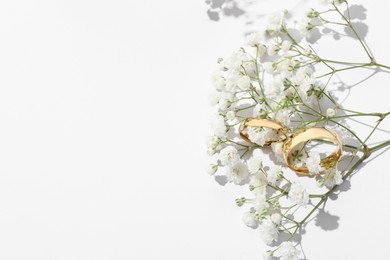 Photo of Golden wedding rings and flowers on white background, above view. Space for text