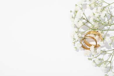 Photo of Golden wedding rings and flowers on white background, space for text