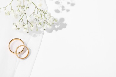 Photo of Golden wedding rings, veil and flowers on white background, top view. Space for text