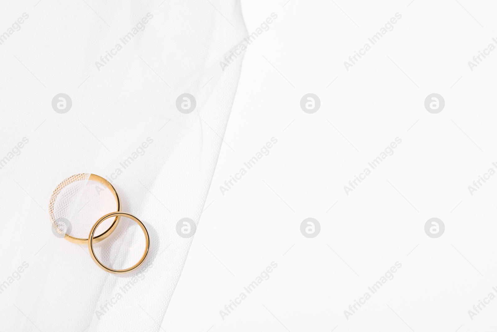 Photo of Golden wedding rings and veil on white background, top view. Space for text