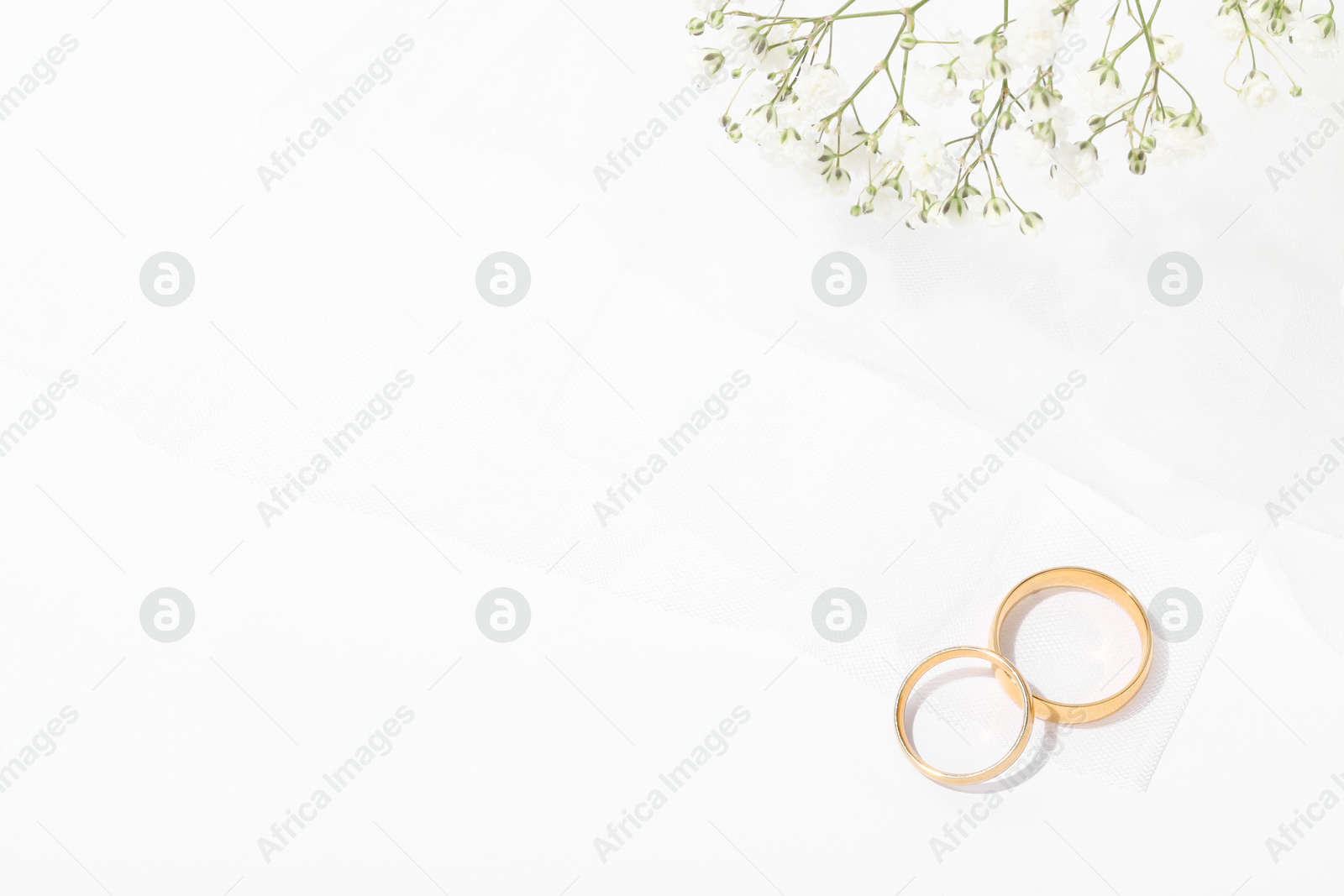 Photo of Golden wedding rings, veil and flowers on white background, top view. Space for text