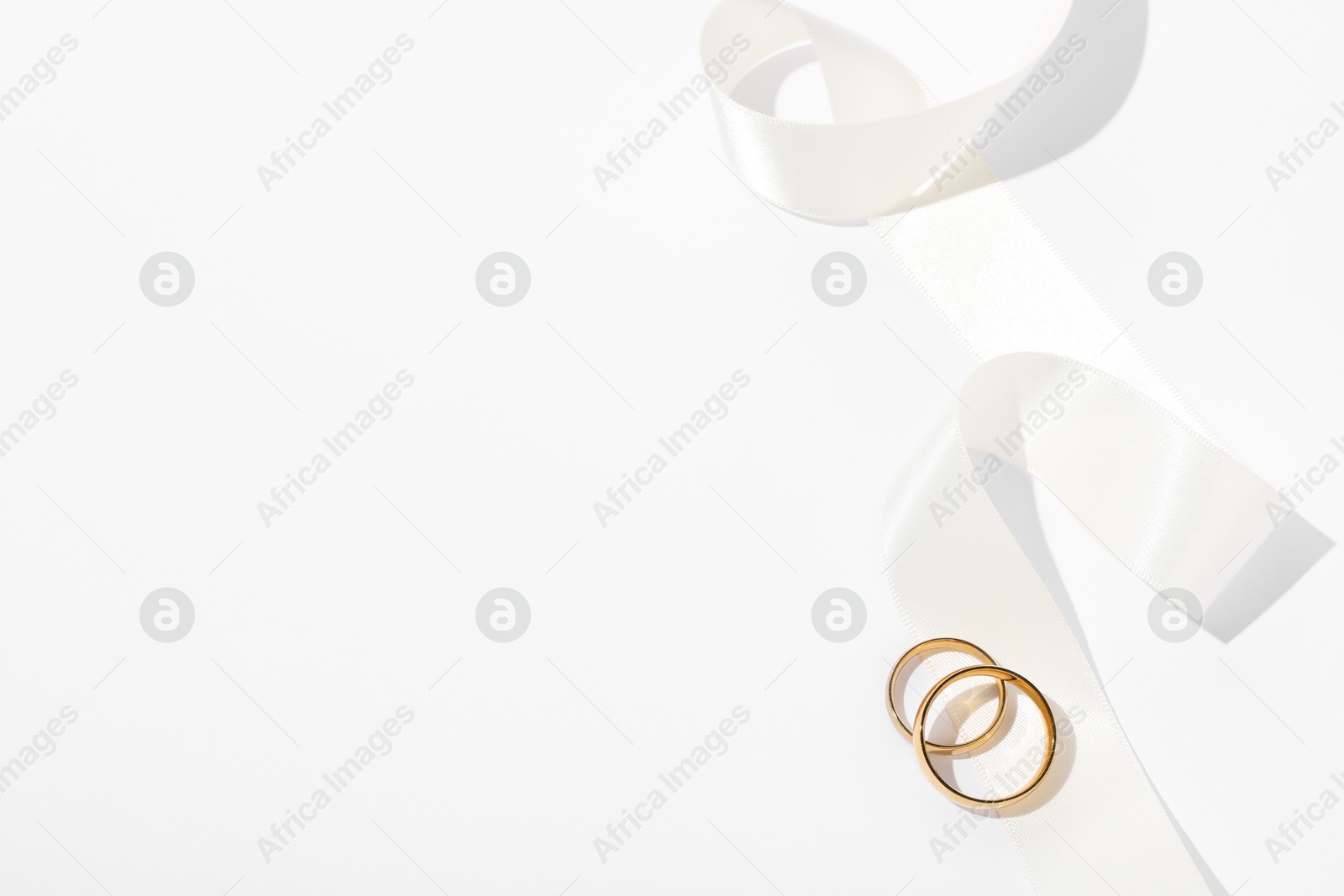 Photo of Golden wedding rings and ribbon on white background, top view. Space for text