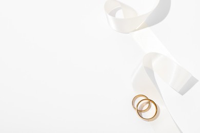 Golden wedding rings and ribbon on white background, top view. Space for text