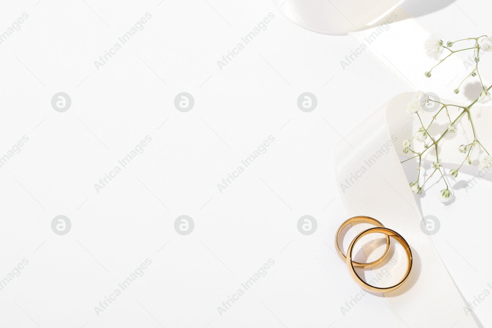 Photo of Golden wedding rings, ribbon and flowers on white background, above view. Space for text