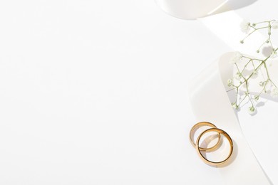 Photo of Golden wedding rings, ribbon and flowers on white background, above view. Space for text