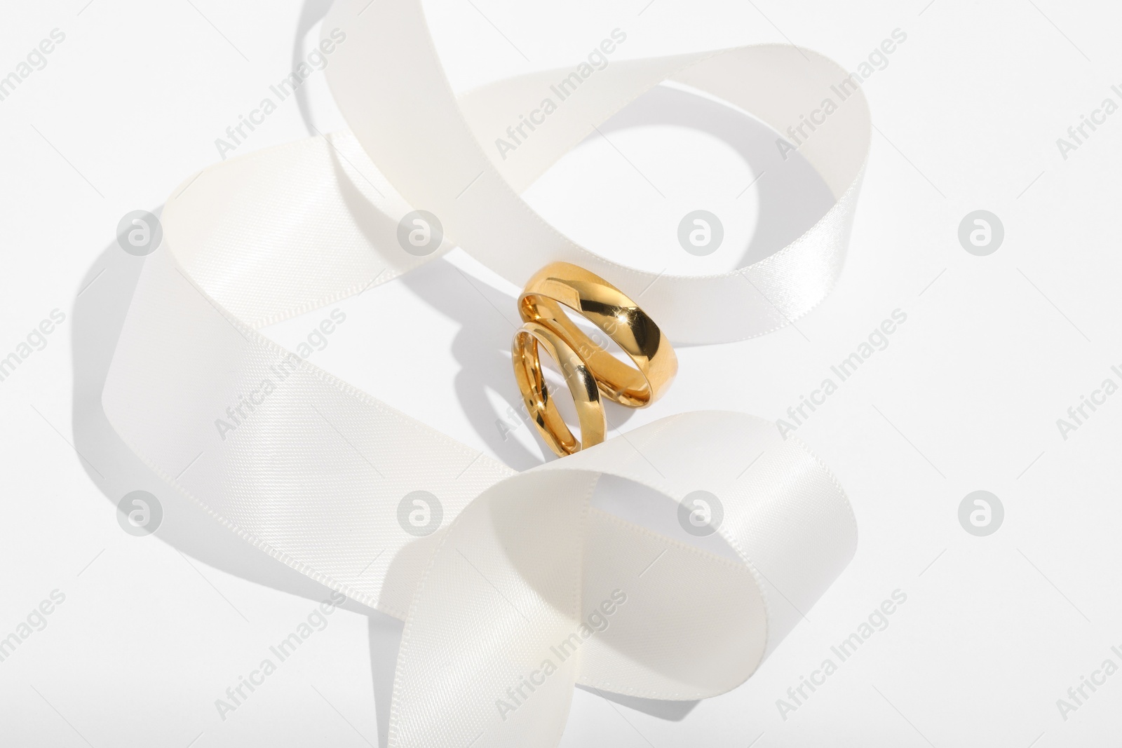 Photo of Golden wedding rings and ribbon on white background, closeup