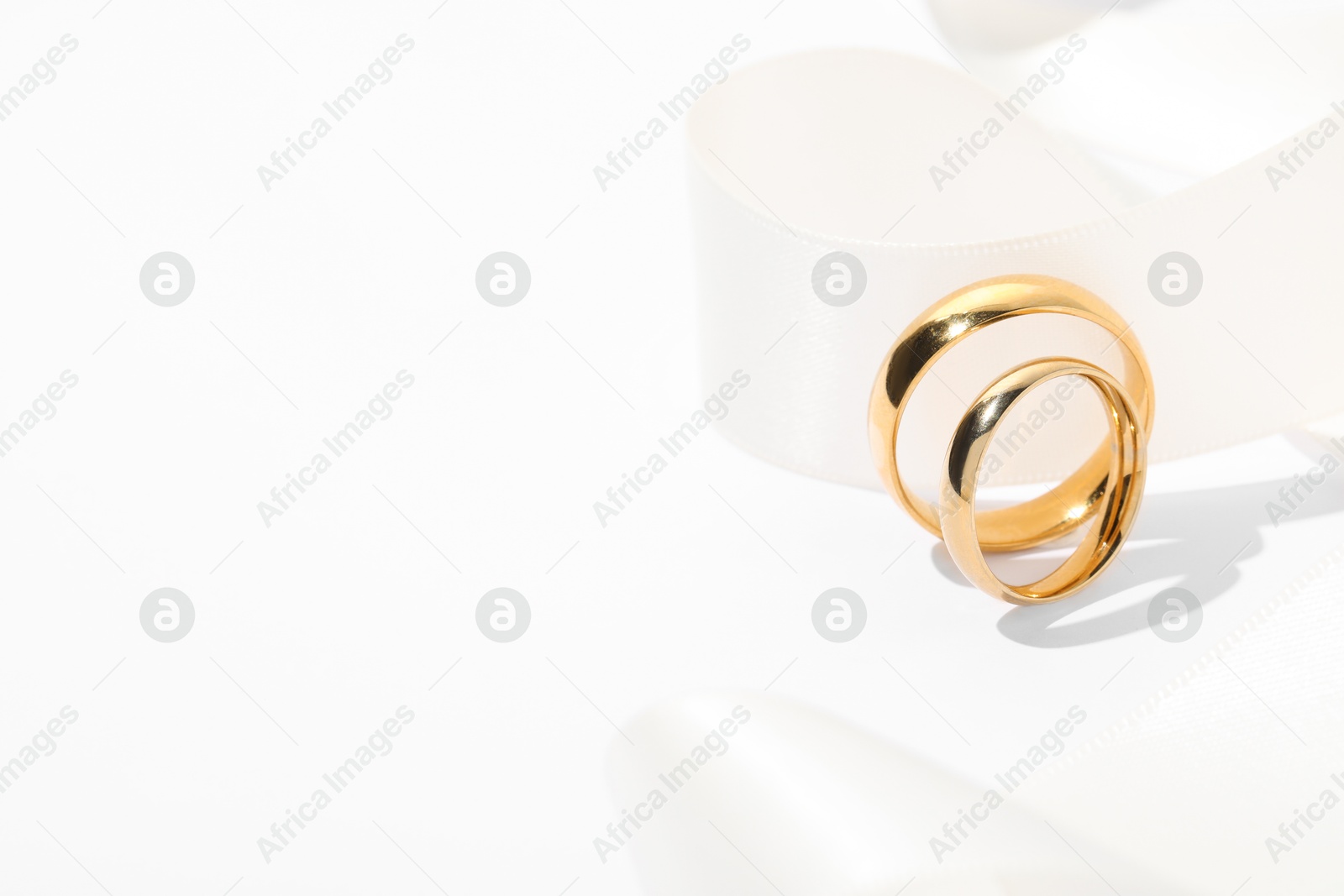 Photo of Golden wedding rings and ribbon on white background, closeup. Space for text