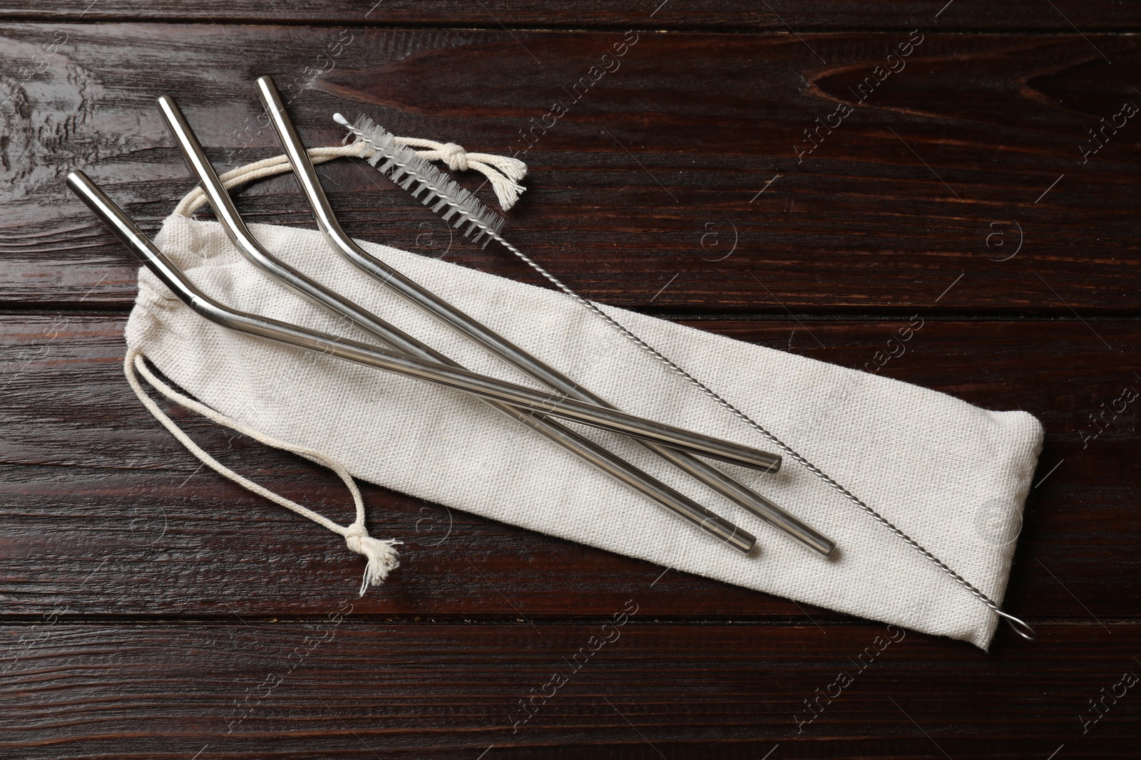 Photo of Metal drinking straws, cleaning brush and bag on wooden table, top view