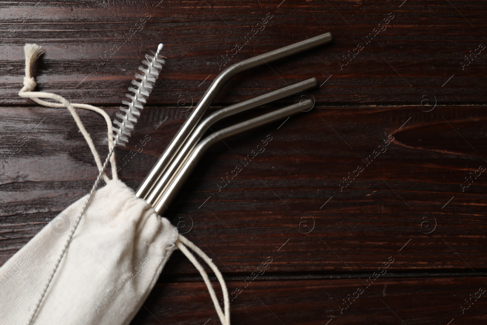 Photo of Metal drinking straws, cleaning brush and bag on wooden table, top view. Space for text