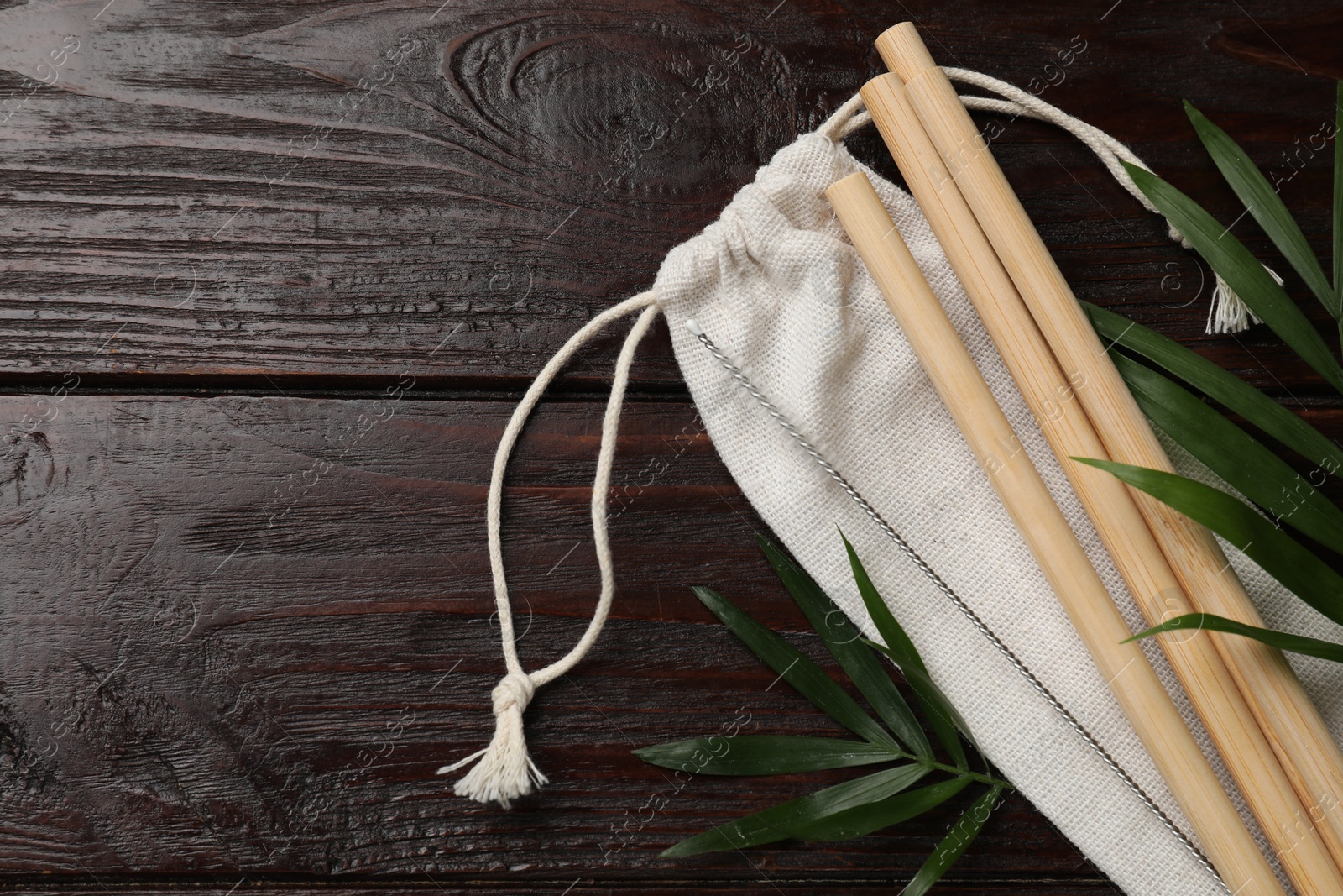 Photo of Bamboo drinking straws, cleaning brush, palm leaves and bag on wooden table, top view. Space for text