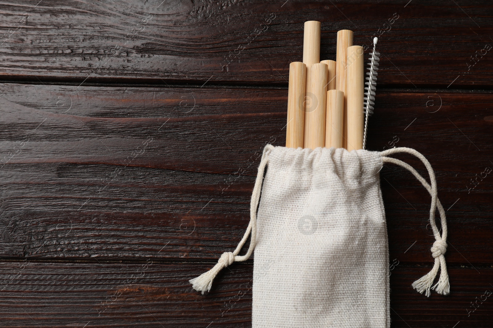 Photo of Bamboo drinking straws and cleaning brush in bag on wooden table, top view. Space for text