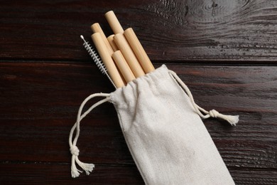 Photo of Bamboo drinking straws and cleaning brush in bag on wooden table, top view