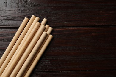 Photo of Bamboo drinking straws on wooden table, top view. Space for text