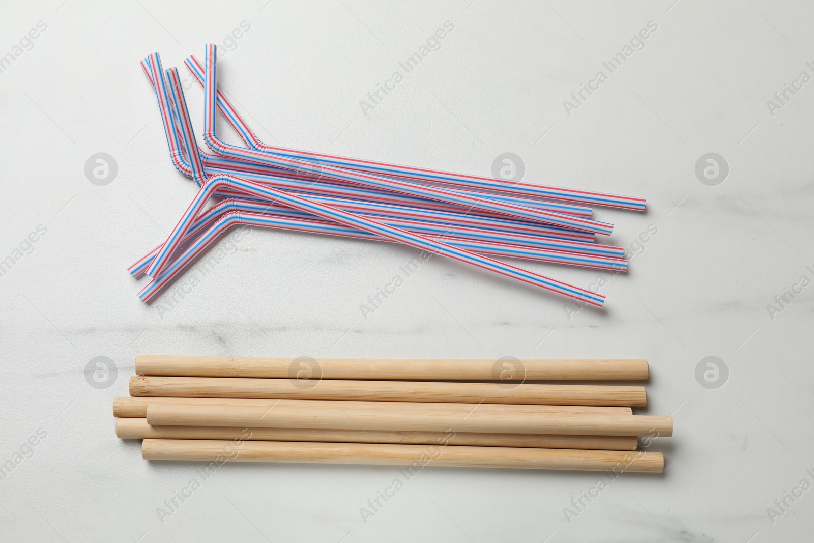 Photo of Plastic and bamboo drinking straws on white marble table, flat lay