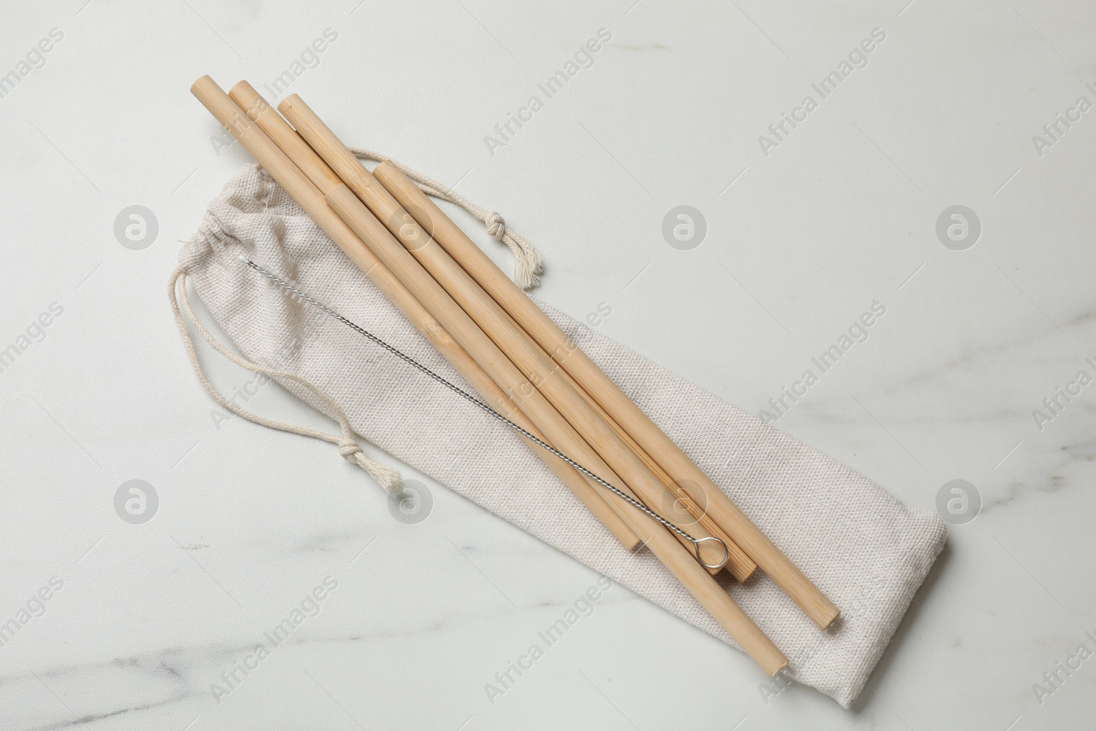 Photo of Bamboo drinking straws, cleaning brush and bag on white marble table, top view