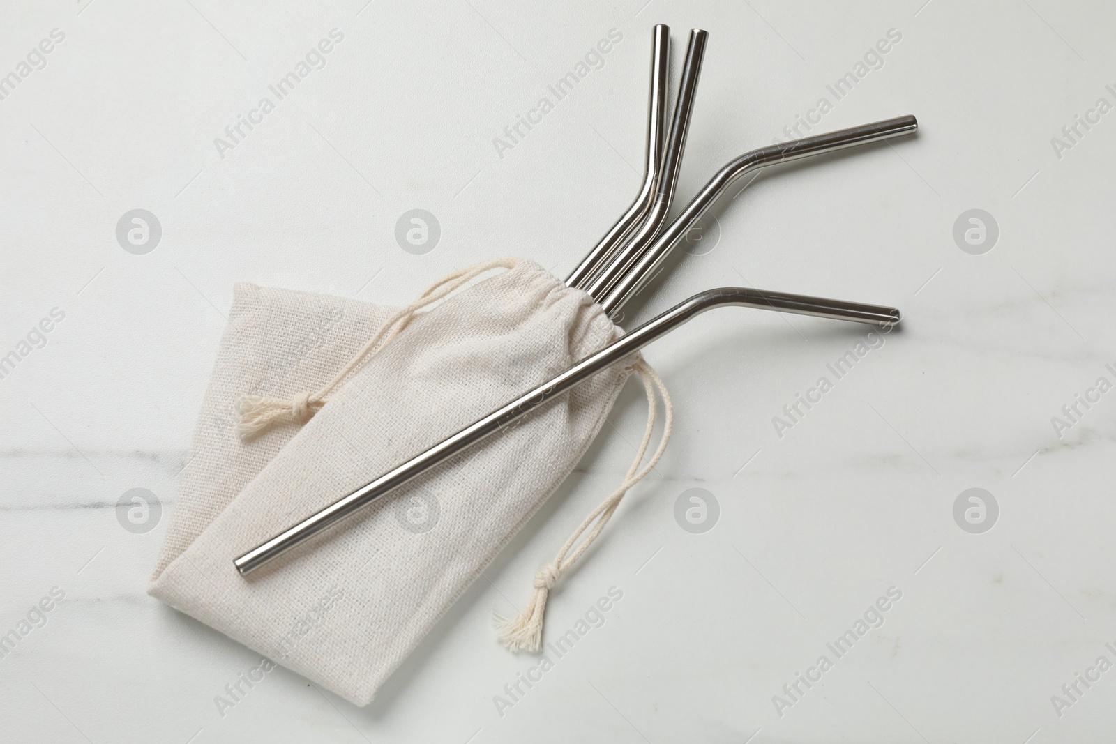 Photo of Metal drinking straws and bag on white marble table, top view