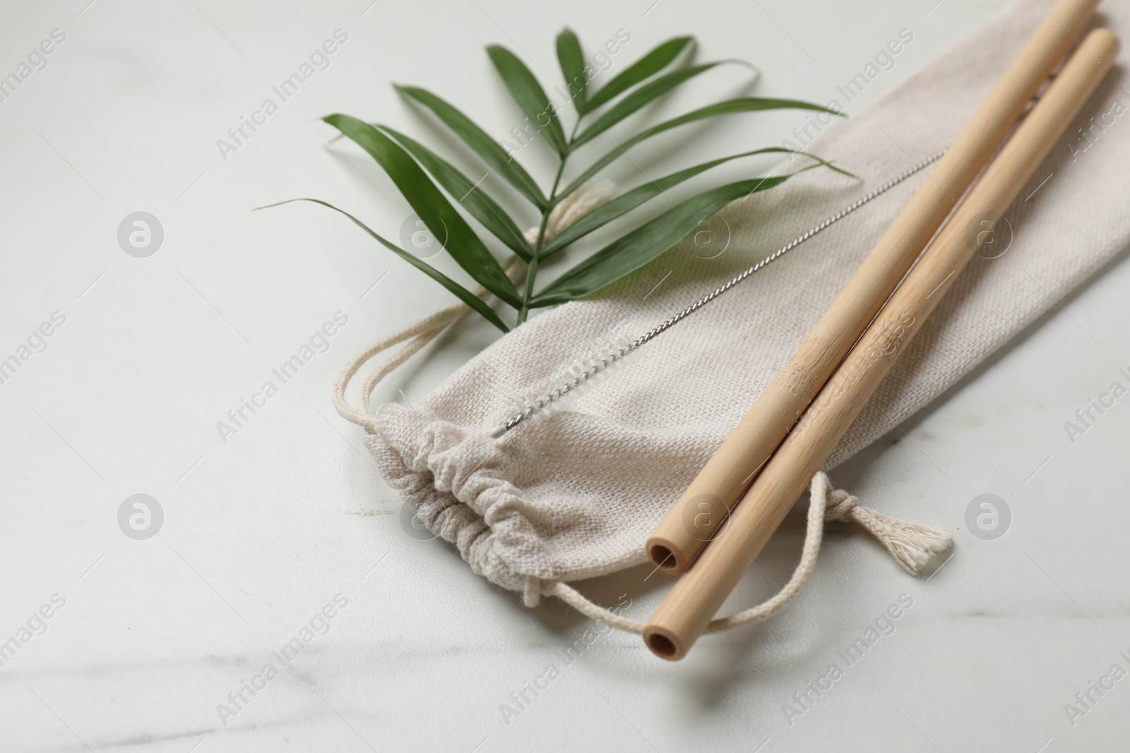 Photo of Bamboo drinking straws, cleaning brush and bag on white marble table, closeup