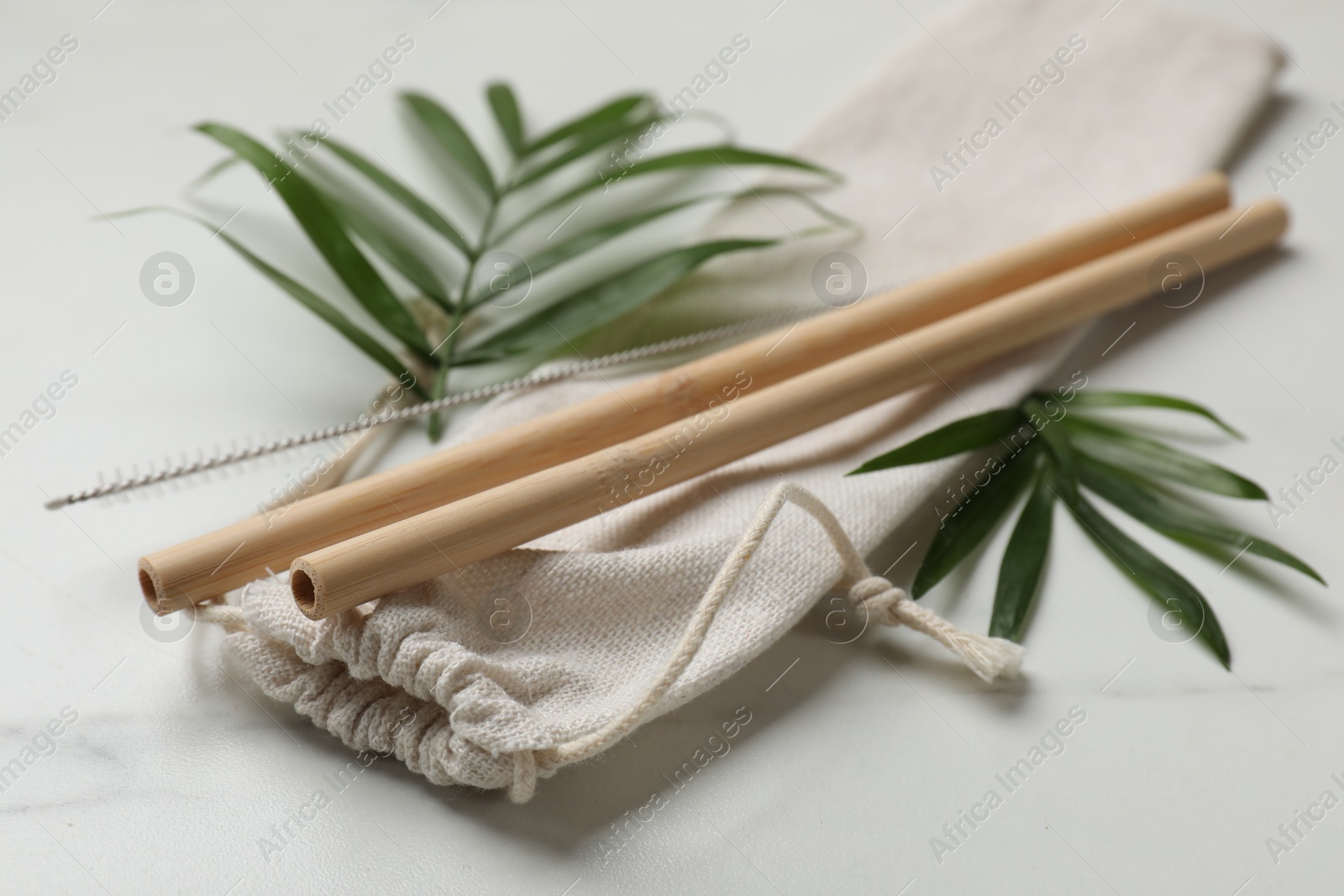 Photo of Bamboo drinking straws, cleaning brush and bag on white marble table, closeup