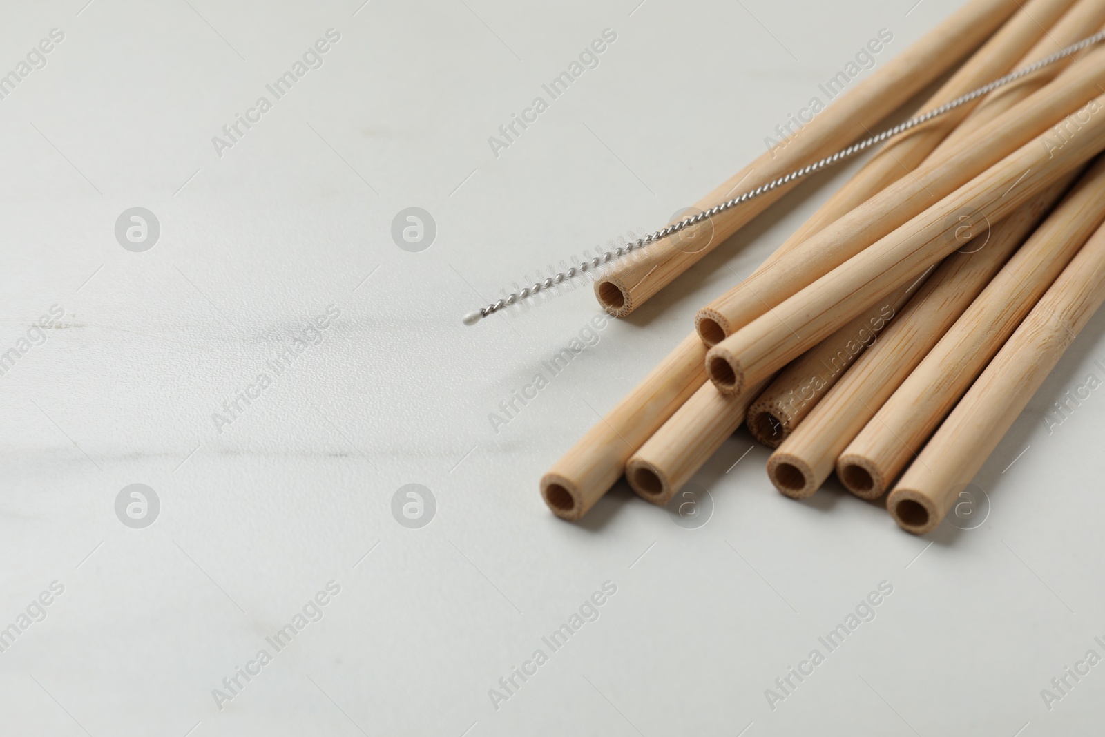 Photo of Bamboo drinking straws and cleaning brush on white marble table, closeup. Space for text