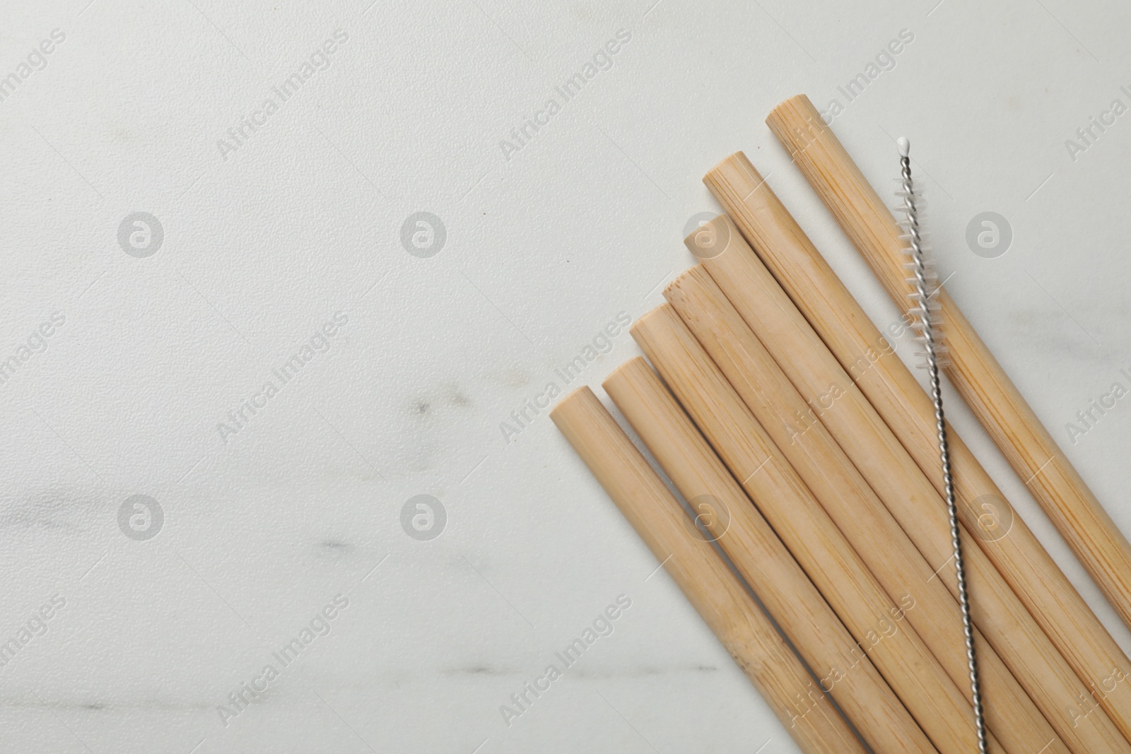 Photo of Bamboo drinking straws and cleaning brush on white marble table, top view. Space for text