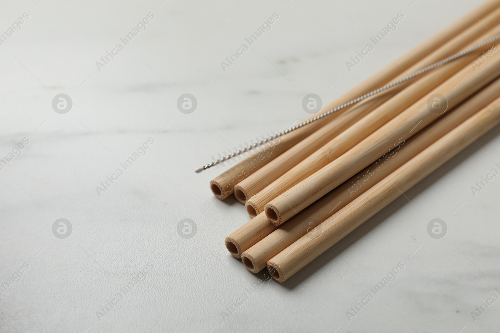 Photo of Bamboo drinking straws and cleaning brush on white marble table, closeup. Space for text