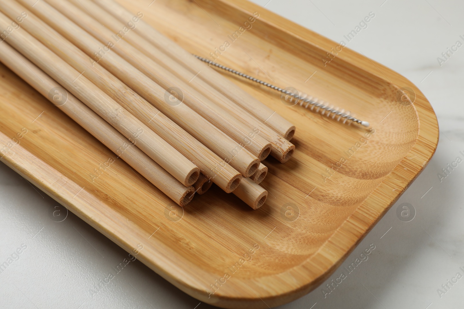 Photo of Bamboo drinking straws and cleaning brush on white marble table, closeup