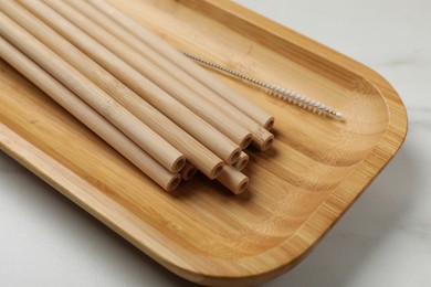 Photo of Bamboo drinking straws and cleaning brush on white marble table, closeup