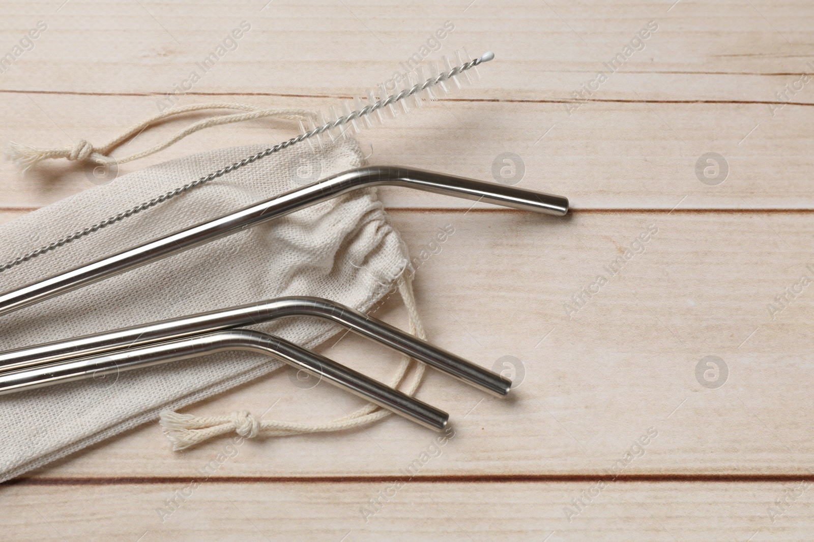 Photo of Metal drinking straws, cleaning brush and bag on wooden table, top view. Space for text