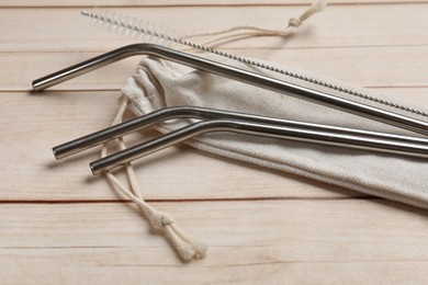 Photo of Metal drinking straws, cleaning brush and bag on wooden table, closeup