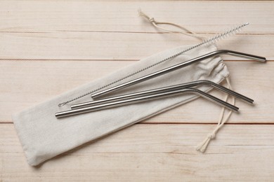 Photo of Metal drinking straws, cleaning brush and bag on wooden table, top view