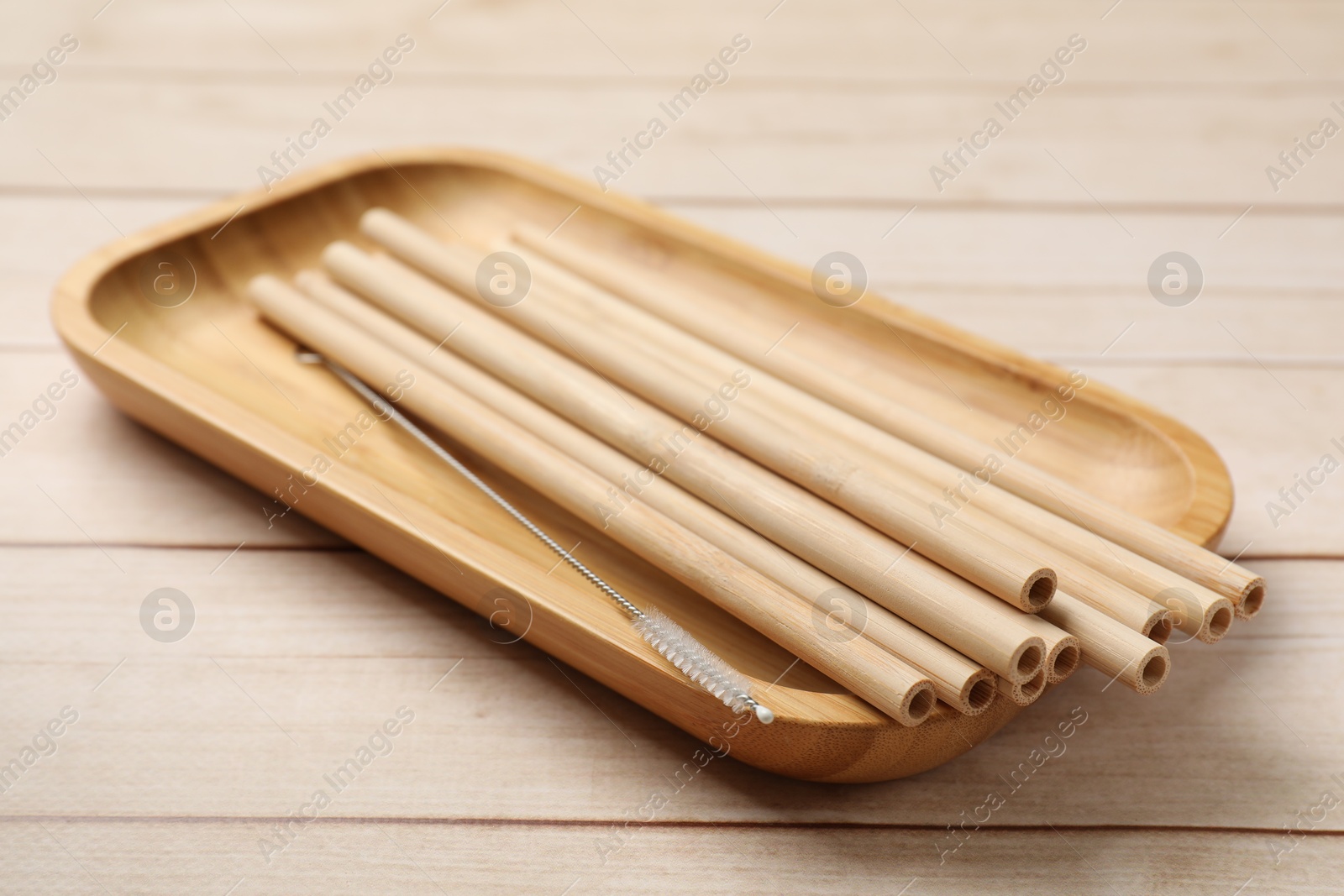 Photo of Bamboo drinking straws and cleaning brush in tray on wooden table, closeup