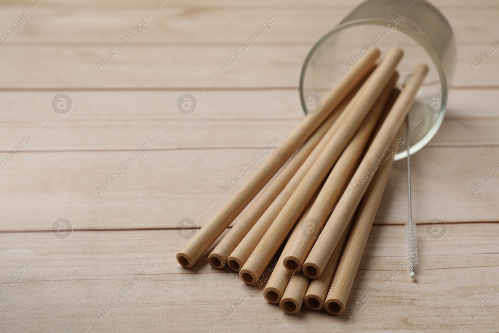 Photo of Bamboo drinking straws and cleaning brush on wooden table, closeup. Space for text