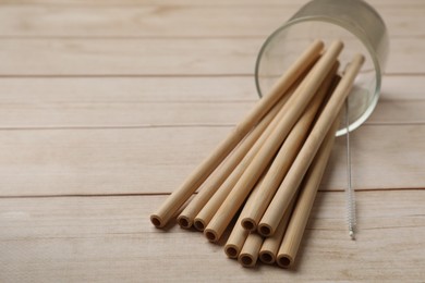 Photo of Bamboo drinking straws and cleaning brush on wooden table, closeup. Space for text