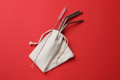 Photo of Metal drinking straws and cleaning brush in bag on red background, top view