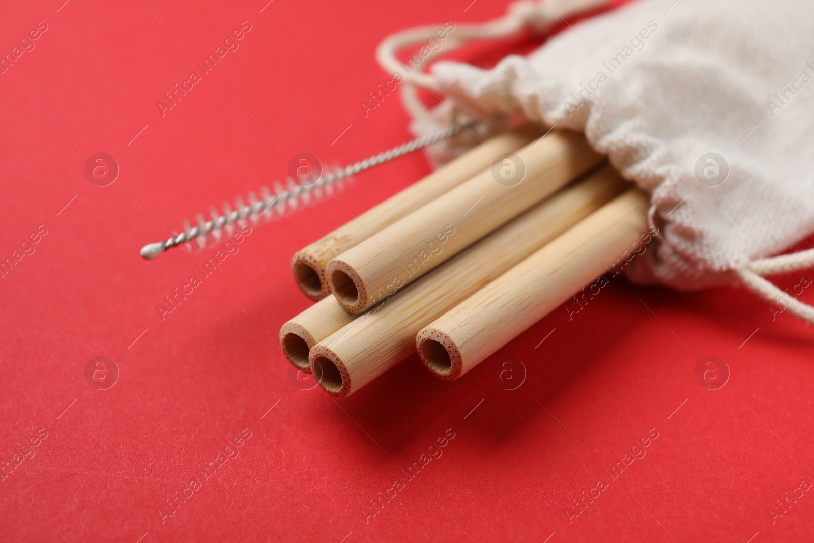 Photo of Bamboo drinking straws and cleaning brush in bag on red background, closeup