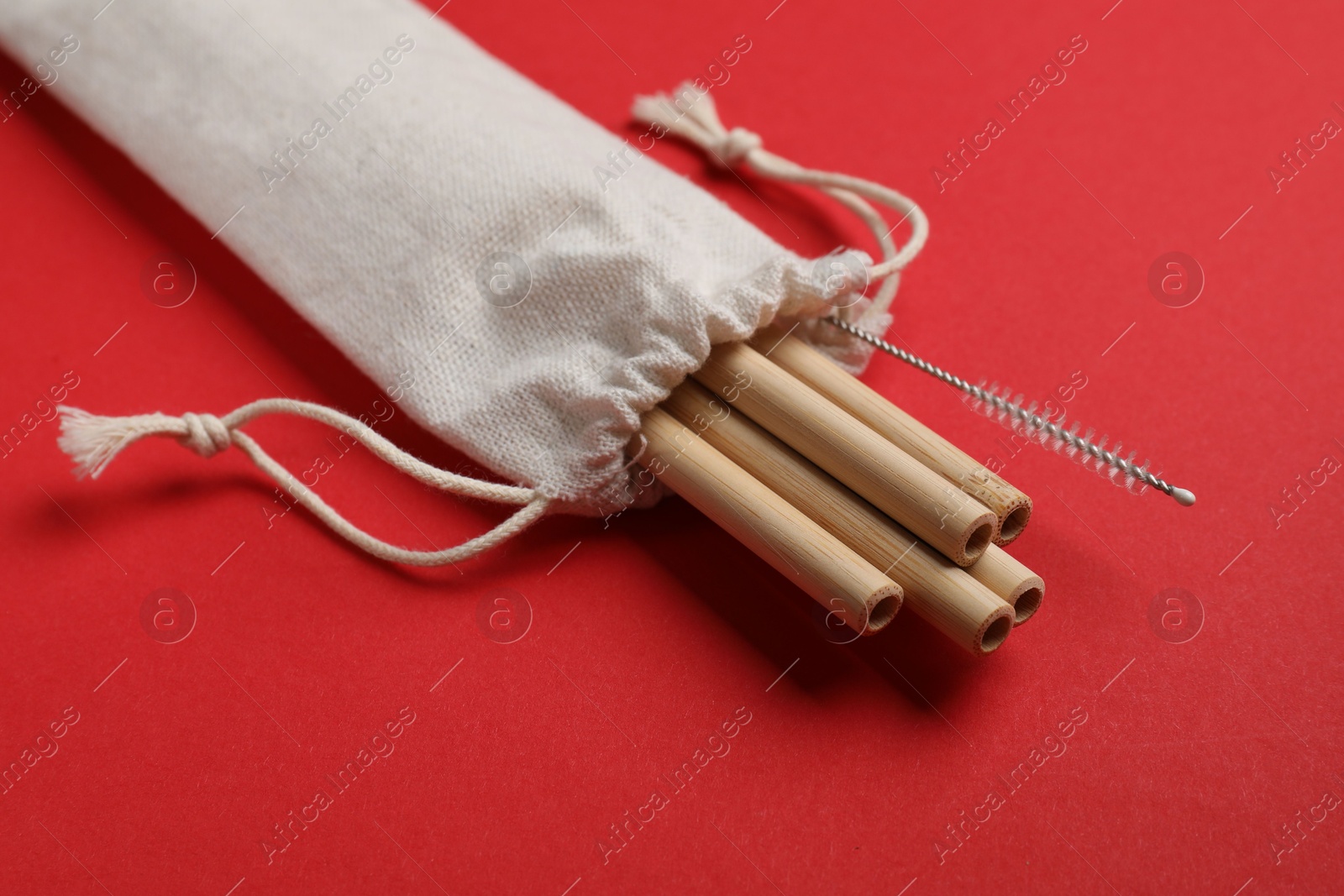 Photo of Bamboo drinking straws and cleaning brush in bag on red background, closeup