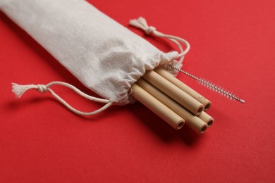 Photo of Bamboo drinking straws and cleaning brush in bag on red background, closeup