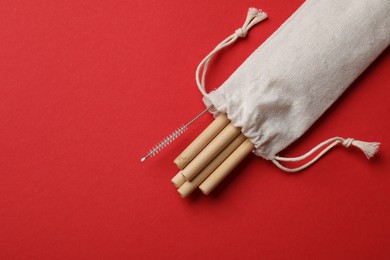 Photo of Bamboo drinking straws and cleaning brush in bag on red background, top view. Space for text