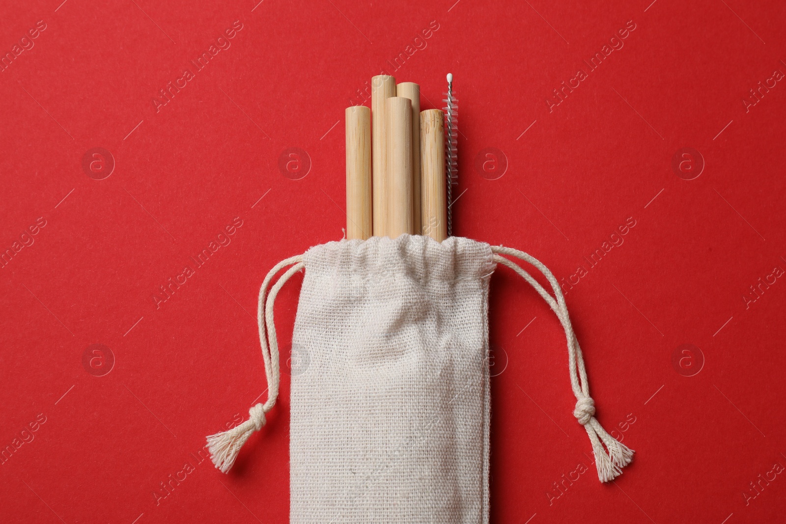 Photo of Bamboo drinking straws and cleaning brush in bag on red background, top view